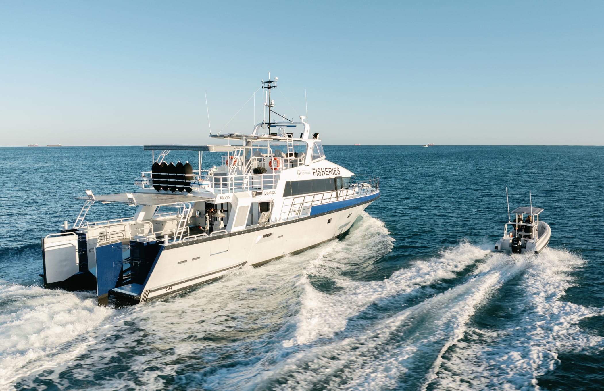 PV Equinox and its RIB tender underway alongside each other, viewed from aft with separate wakes and the patrol vessel’s stern doors open.